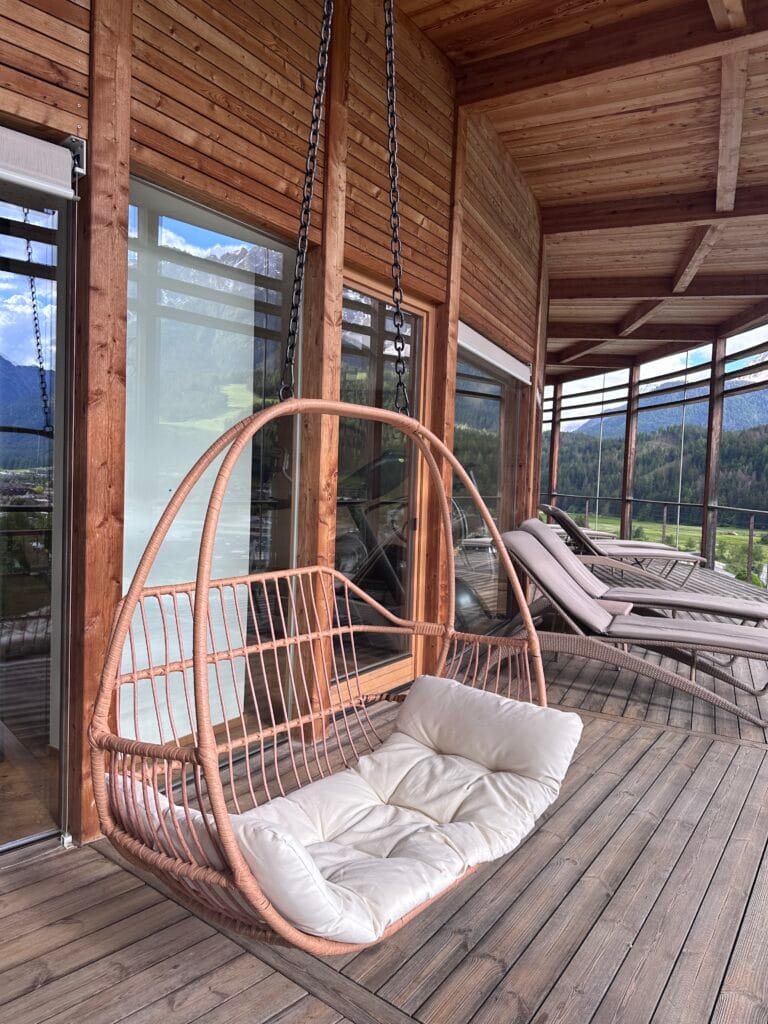 Wooden balcony with loungers and a hanging chair overlooking the mountains at Leitlhof Hotel in South Tyrol.