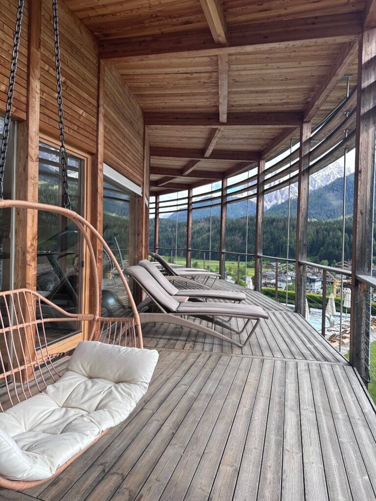 Wooden balcony with loungers and a hanging chair overlooking the mountains at Leitlhof Hotel in South Tyrol.