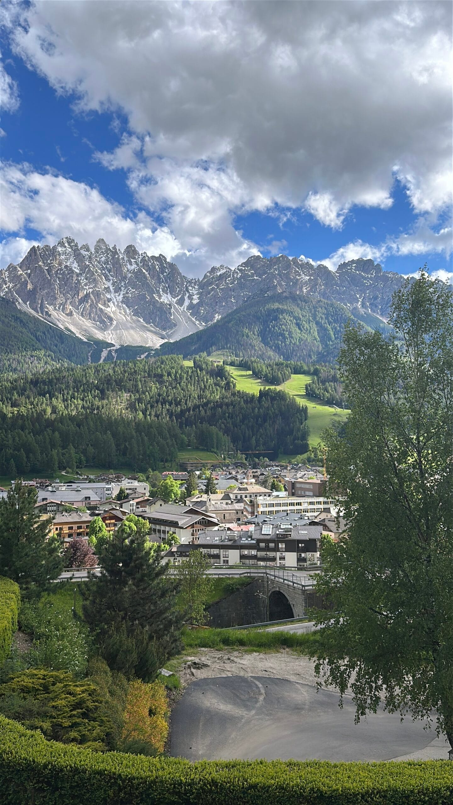 Alpine town of San Candido nestled in a green valley, surrounded by dense forests and dramatic snow-capped peaks of the Dolomites.