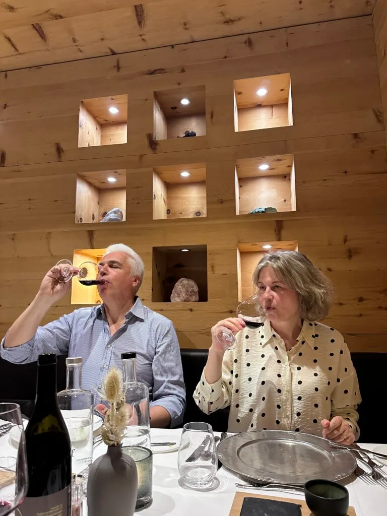 Mature couple enjoying red wine at a wooden-walled restaurant table, surrounded by glasses and decor, inside Leitlhof Hotel in South Tyrol.