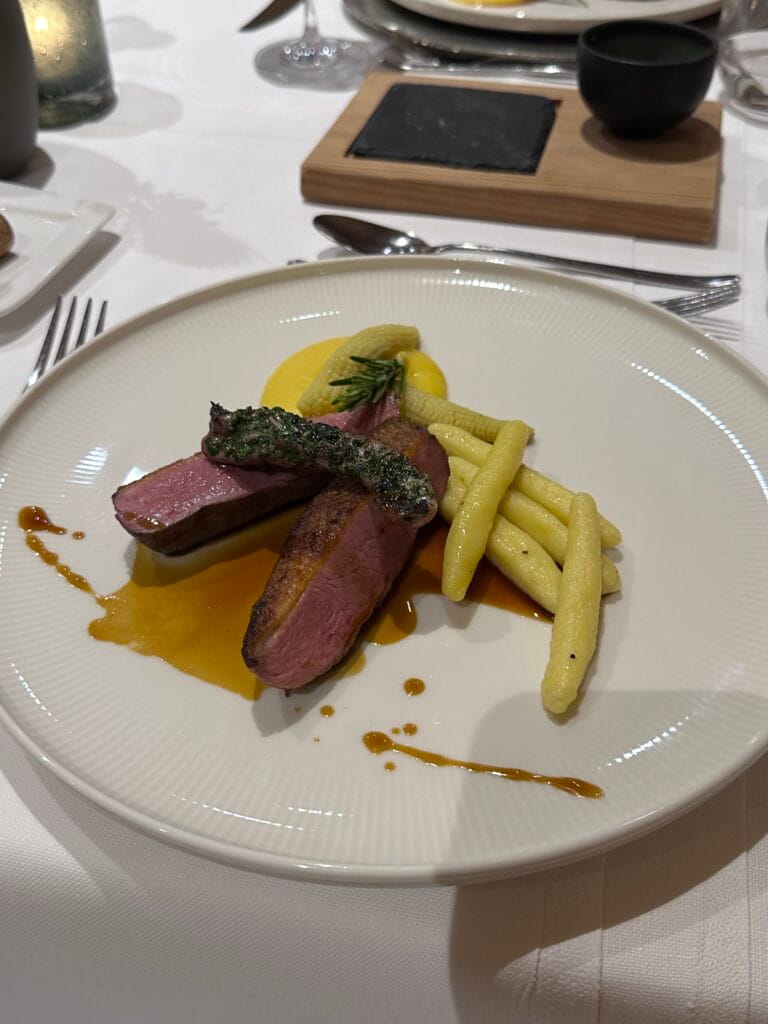 Gourmet plate featuring sliced duck breast with a glaze, yellow string beans, and a herb garnish, served on a white plate.