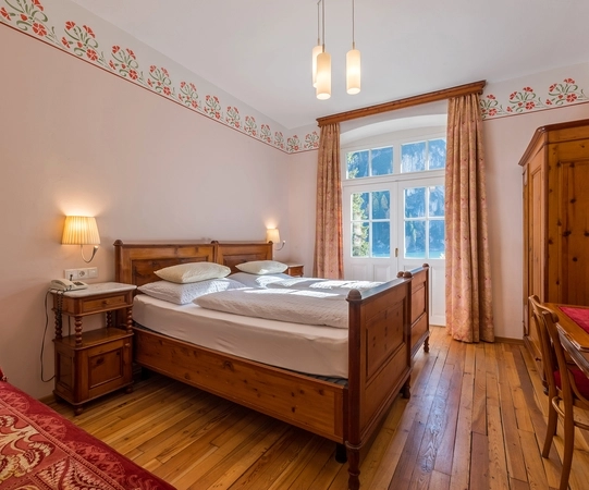 Traditional alpine hotel room with wooden furniture, double bed, and floral decor near Lago di Braies.