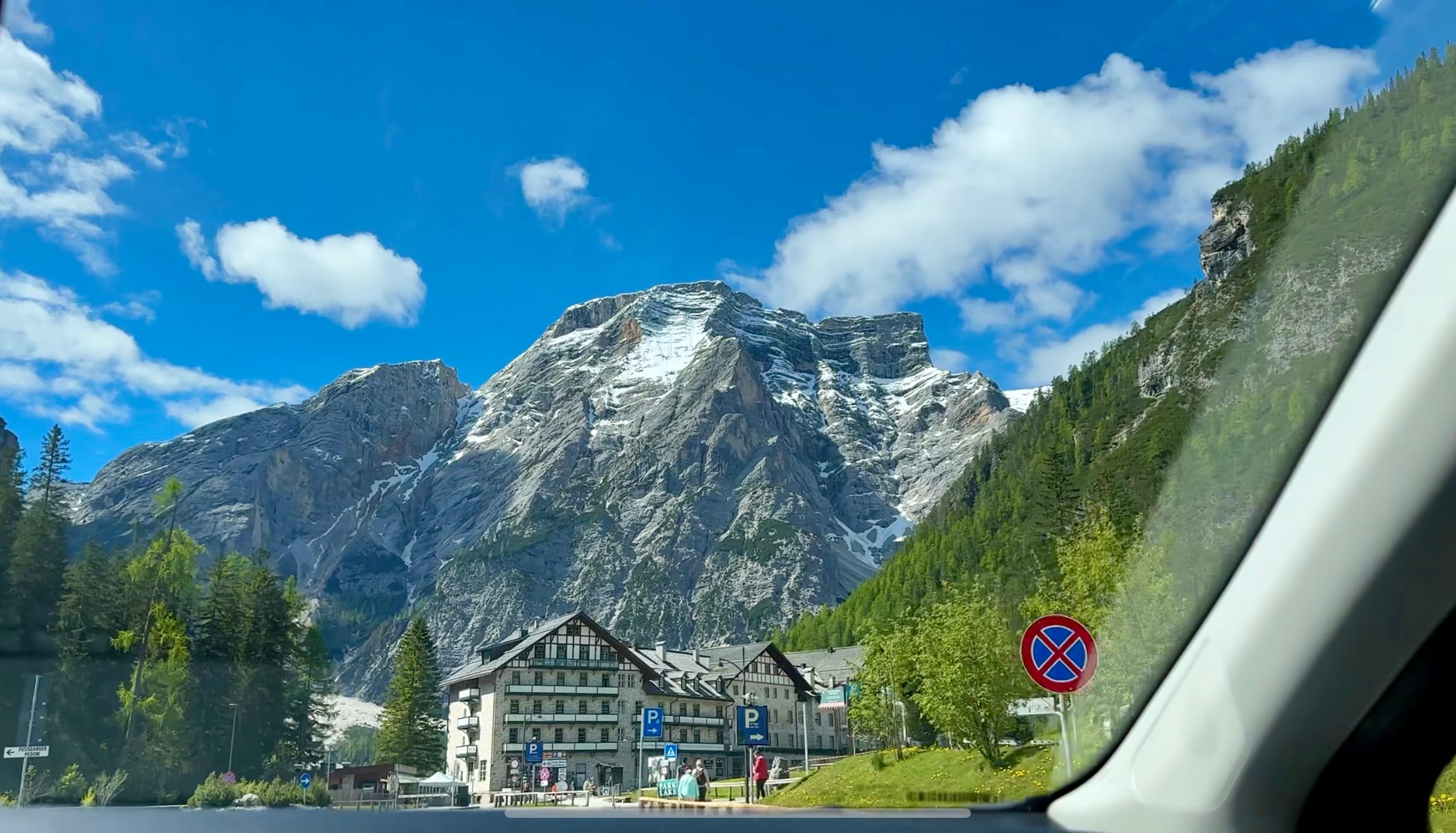 View of snow-capped mountains and Hotel Lago di Braies from inside a car.