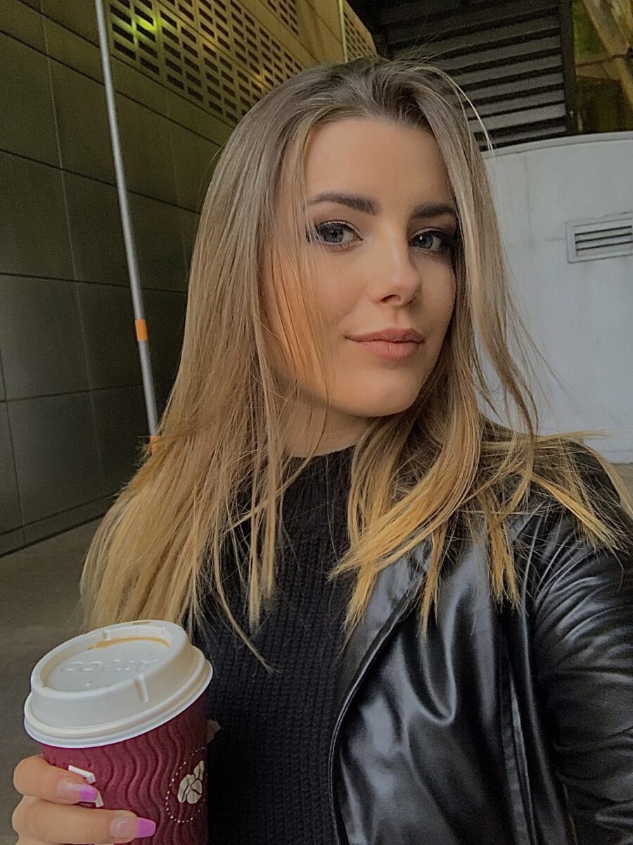 Young woman with blonde hair holding a takeaway coffee cup, stylish black leather jacket.
