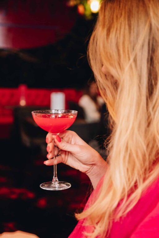A hand holding a pink coupe cocktail at Purgatory Bar