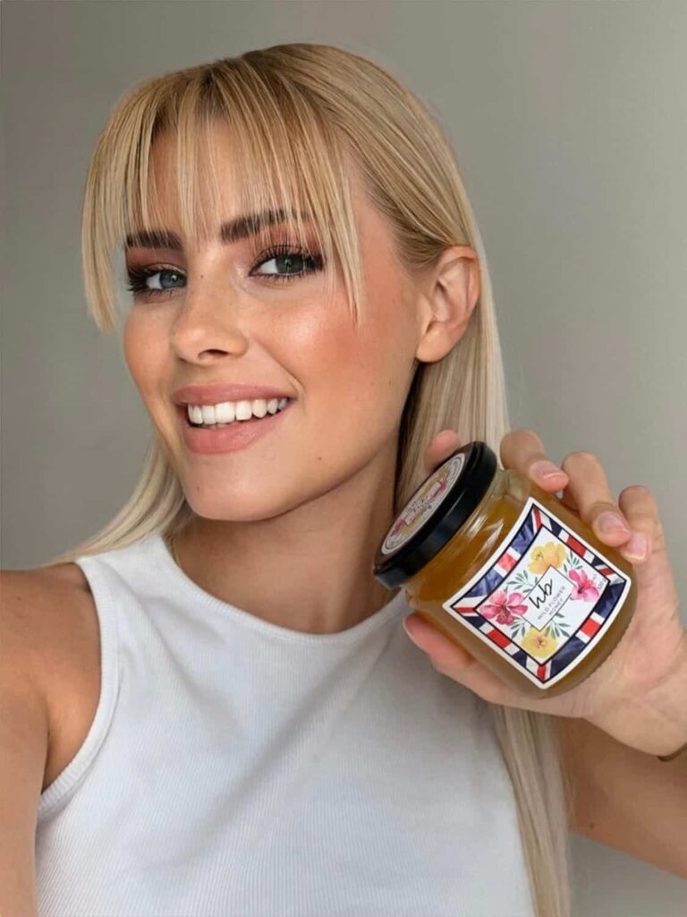 Velena Nikolova with a fringe in a white top holding a jar of Honeybee and Co honey