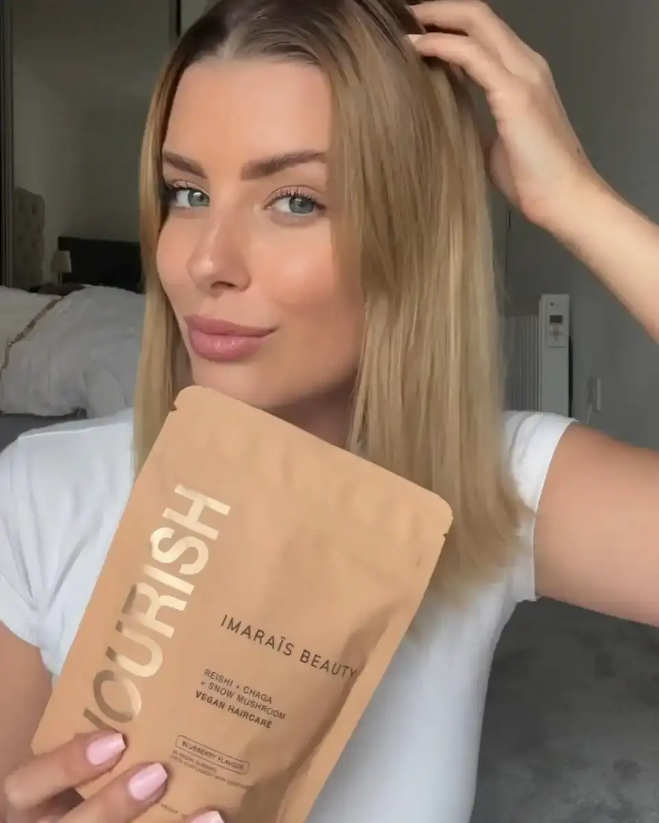 Velena Nikolova in a white T-shirt holding a brown Imarais Beauty Nourish pouch beside her face