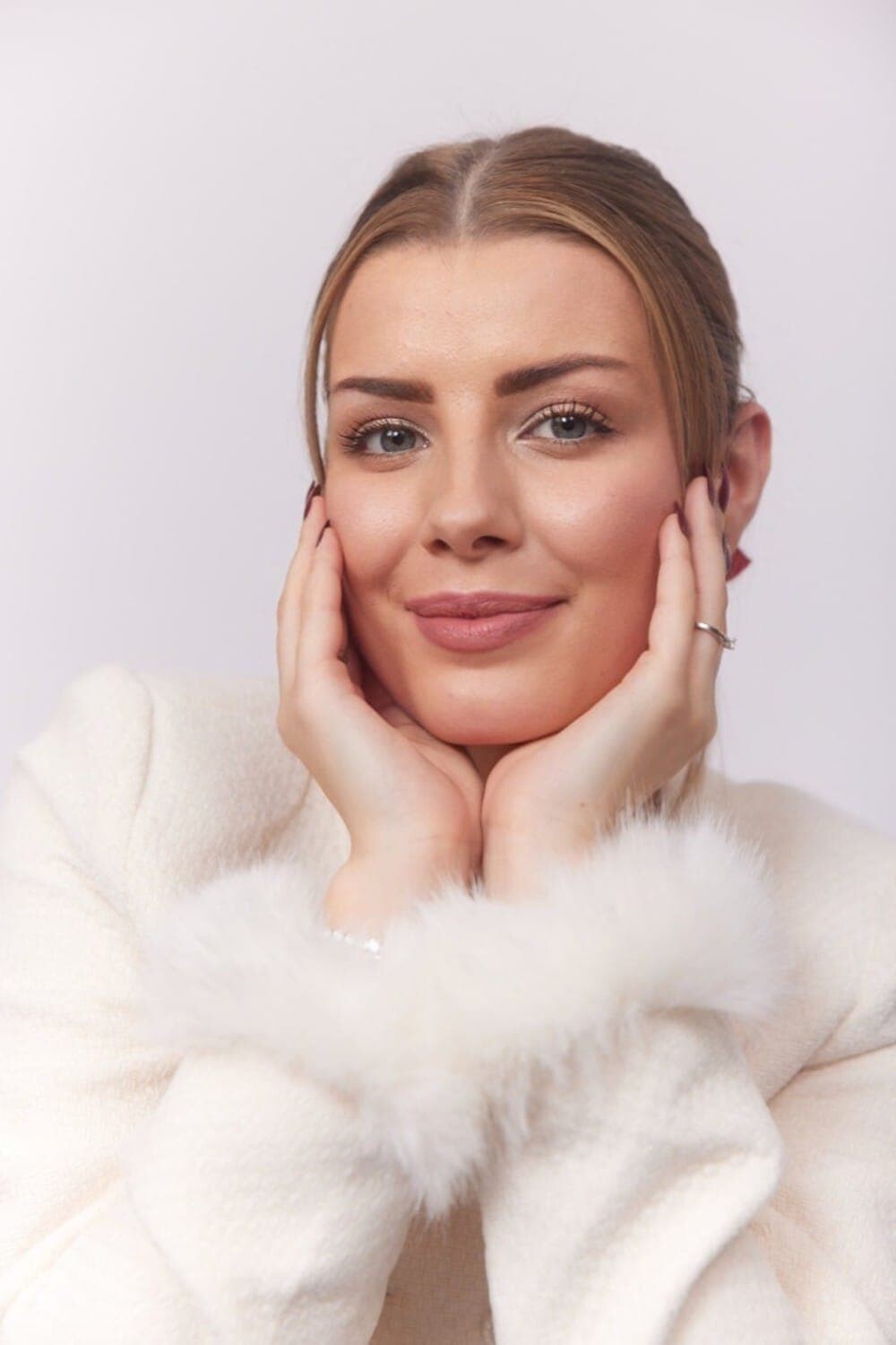 Velena Nikolova in a white fur jacket with her hands on her cheeks