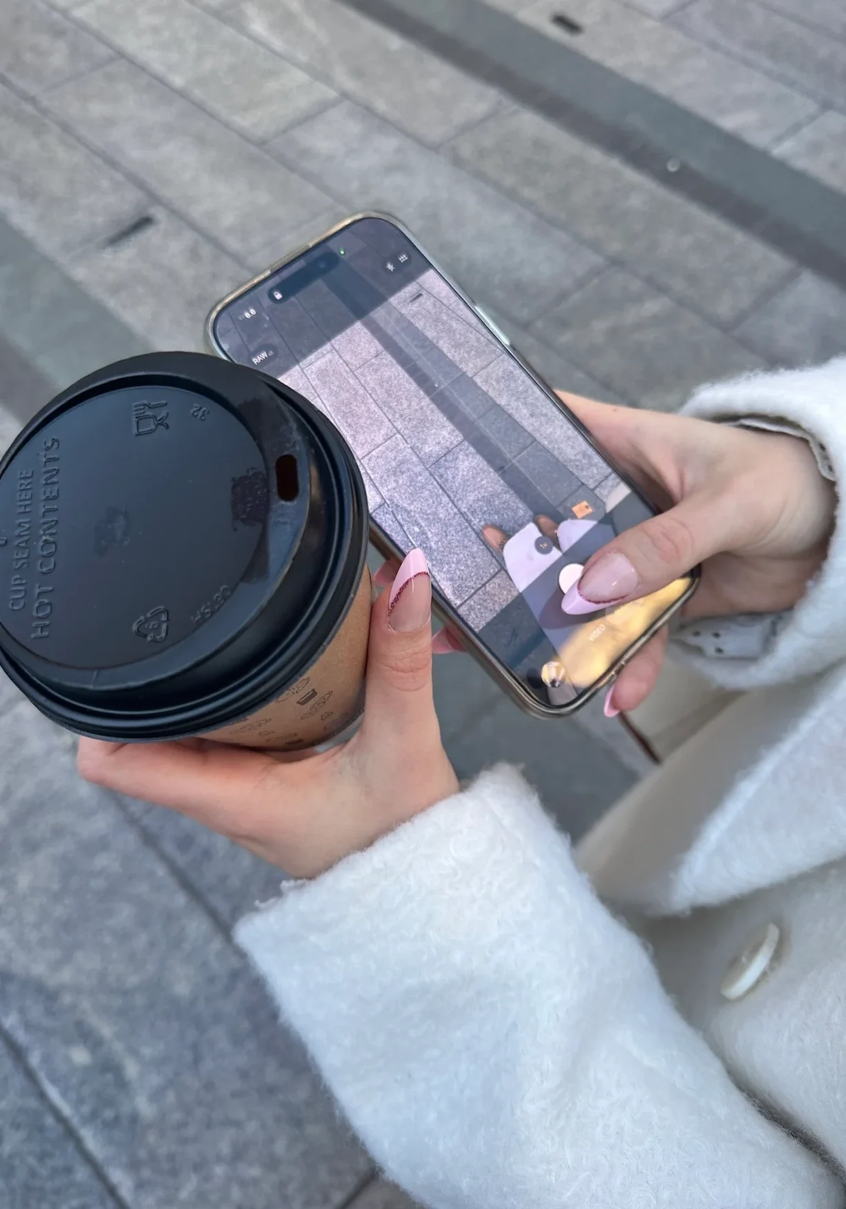 Apps UGC showing a smartphone recording content while holding a takeaway coffee in an everyday city setting
